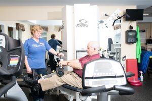 resident exercising on equipment with rehab specialist assiting