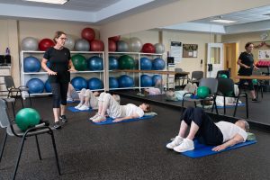 resident and trainer doing floor stretching exerciseson mats