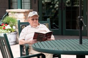 senior resident with baseball cap reading book on the patio